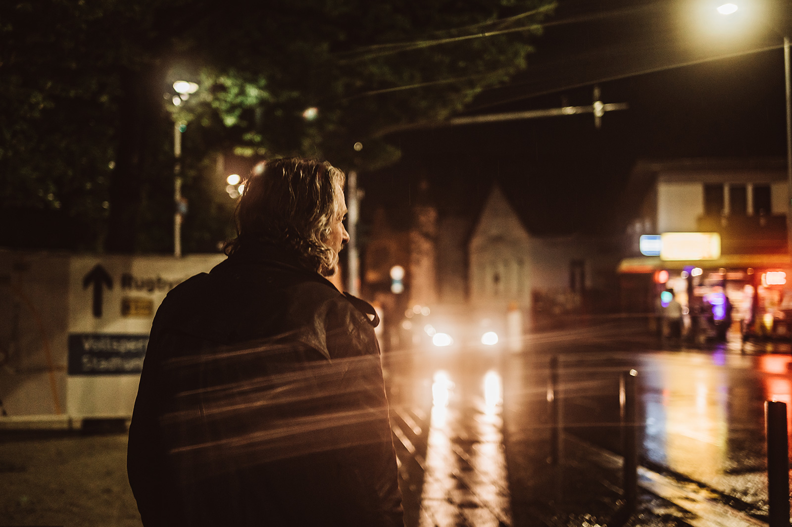 Ray Cooper unterwegs auf der Straße im Regen mit Lichtern von Autos